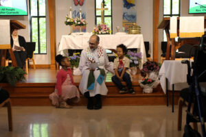 Pastor Chris sits on the chancel steps during worship, smiling and talking with two young children at Holy Covenant UCC.