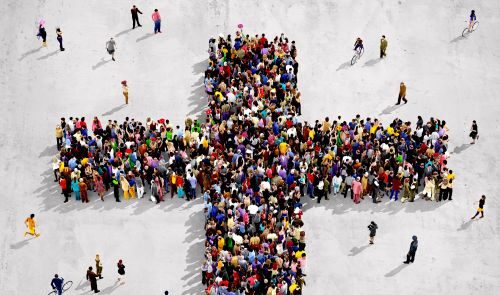 A large, diverse group of people standing together in the shape of a cross on a white concrete background, viewed from above.