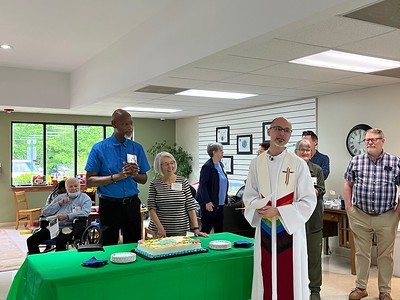 Pastor and congregants gathered around a decorated cake table during a fellowship celebration at Holy Covenant.