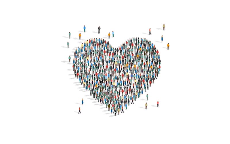 A large, diverse crowd of people arranged in the shape of a heart, symbolizing inclusive community, unity, and shared compassion.