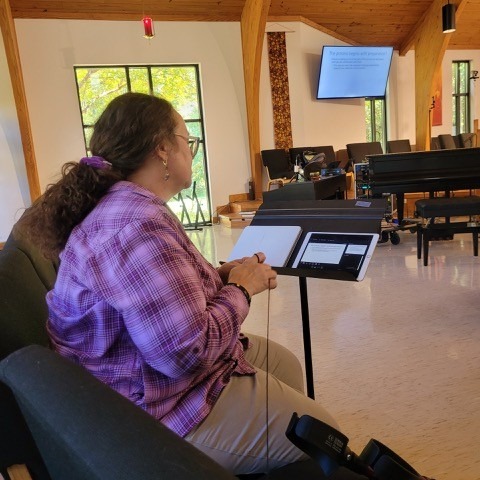 Laura sitting at the front of the sanctuary preparing worship slides at a laptop, with the sanctuary screen visible in the background.