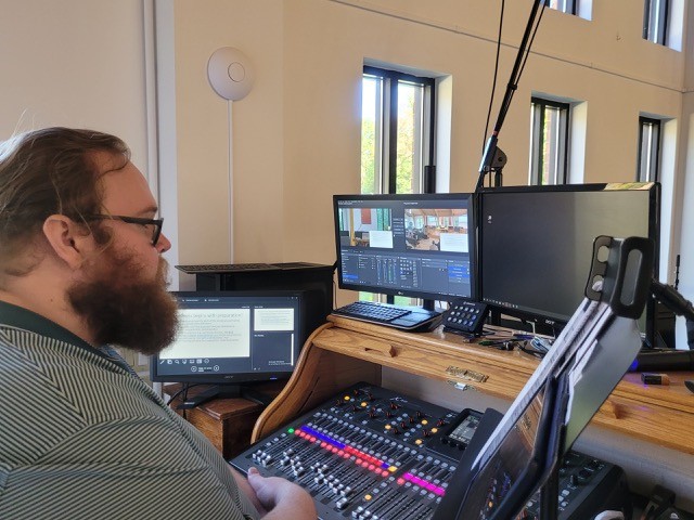 A volunteer operates Holy Covenant’s AV control center, surrounded by sound equipment, multiple monitors, and livestreaming software.