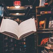An open book appears suspended in midair in a warmly lit library, evoking the power of story and resistance.