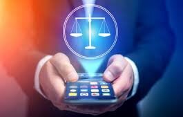 A person in a suit holds a smartphone with a glowing hologram of balanced scales projected above it, symbolizing justice in the digital age.