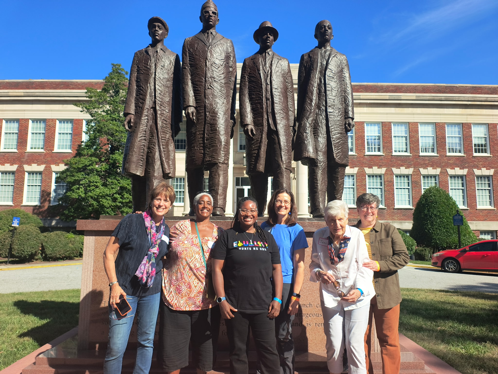 Members of Holy Covenant’s Racial Justice & Equity planners stand before the February One monument at N.C. A&T, smiling in the morning sun — Photo courtesy of Meg Houlihan