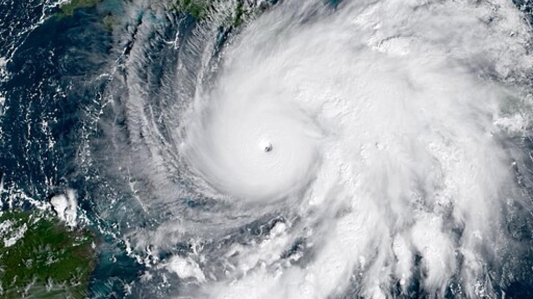 Aerial image showing hurricane damage along a Caribbean coastline with flooded streets and damaged homes.