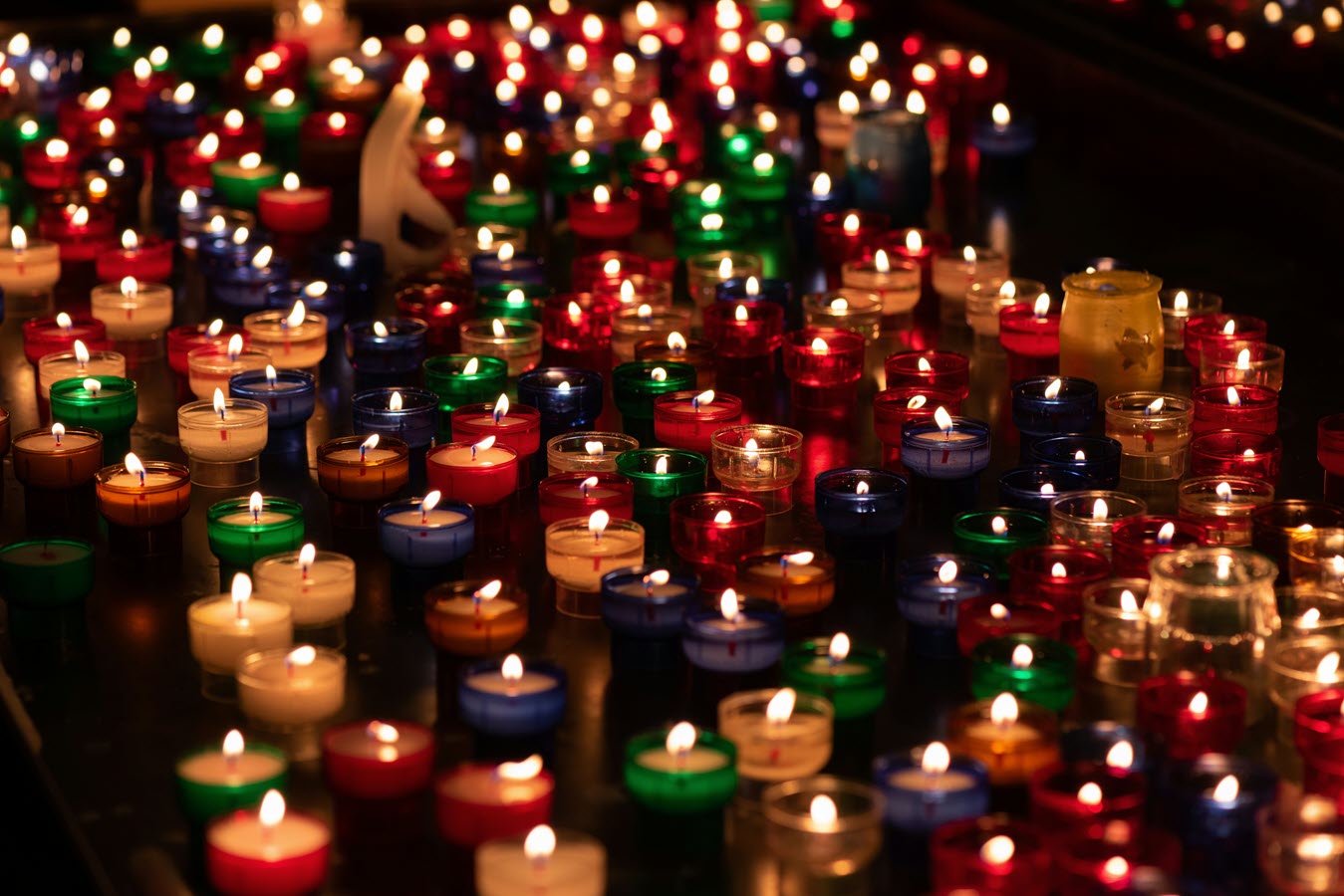 Hundreds of small votive candles glowing warmly in a sanctuary, symbolizing remembrance, prayer, and the enduring light of the saints.